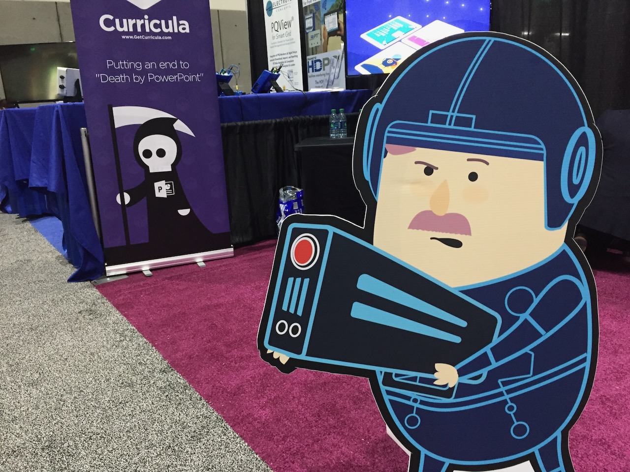 Curricula trade show booth with cartoon mascot and anti-Death by PowerPoint banner